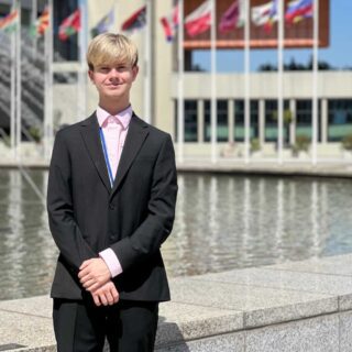 Corey stood in a suit with world flags in the background