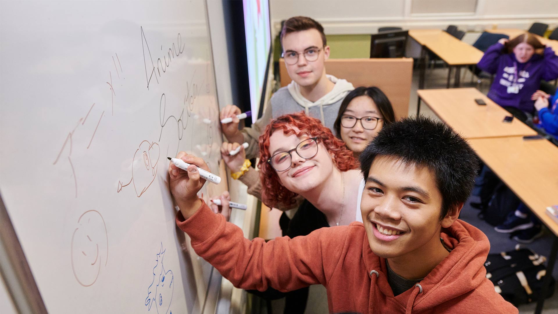 Students working on board in anime society, looking at camera and smiling
