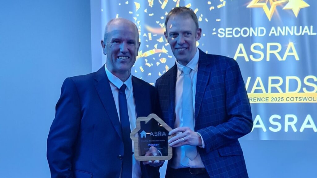 two white men wearing blue suits, holding a glass award for 'Creating Best student homes'