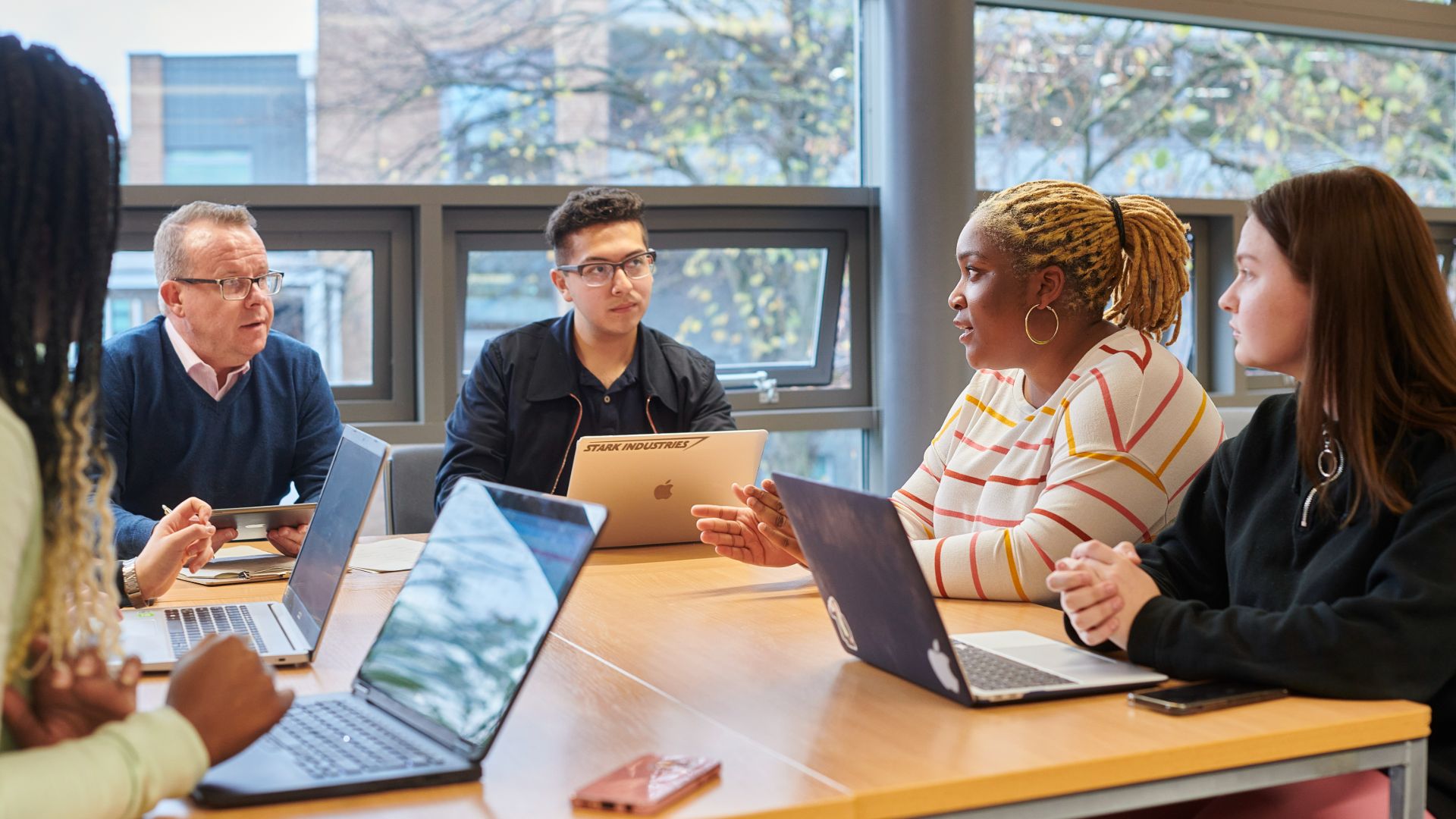 A group of people sitting around a table with laptops