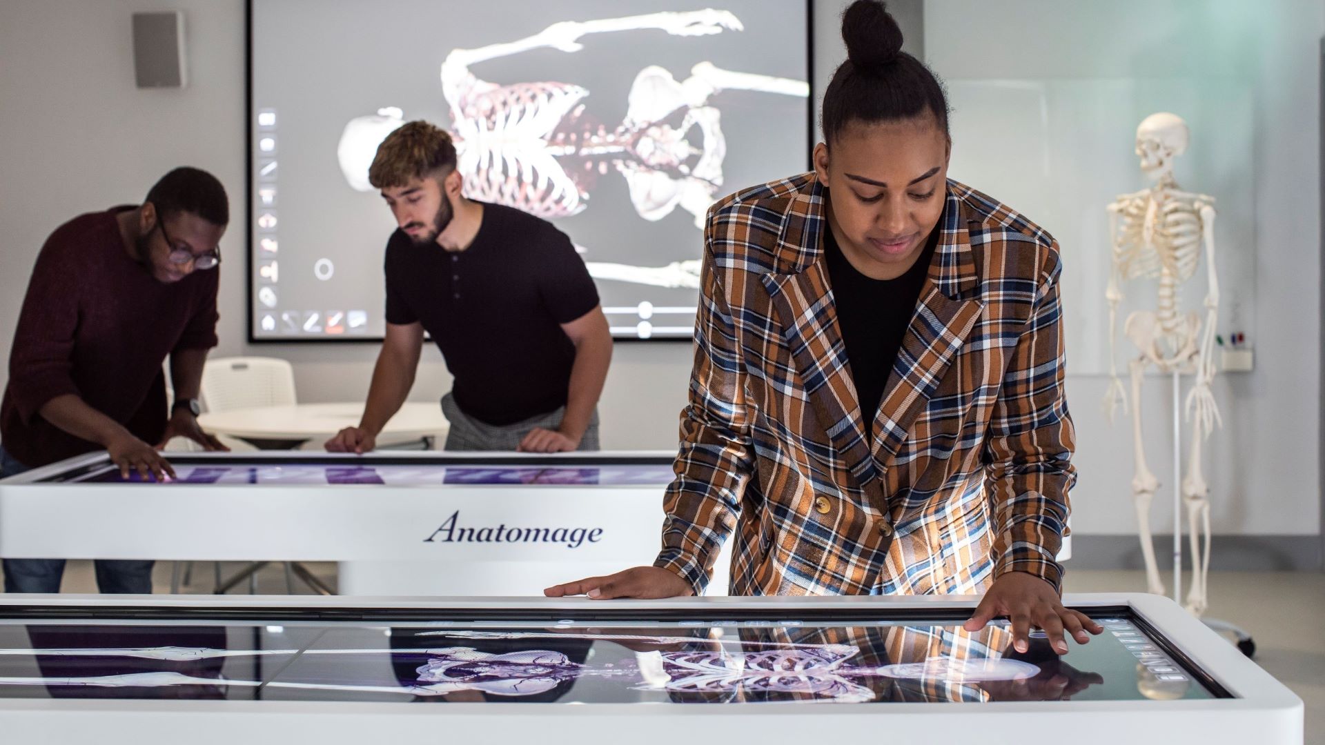 Three Medical School students stand at anatomage tables and touch the screens