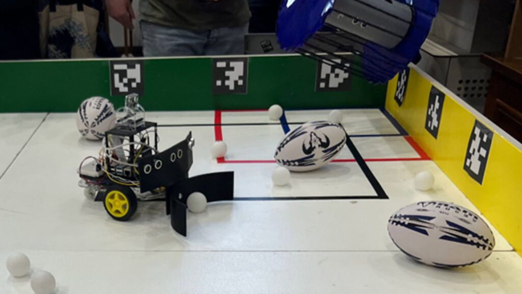 Competition entry for Unibots competition showing a robot surrounded by miniature rugby balls and ping pong balls