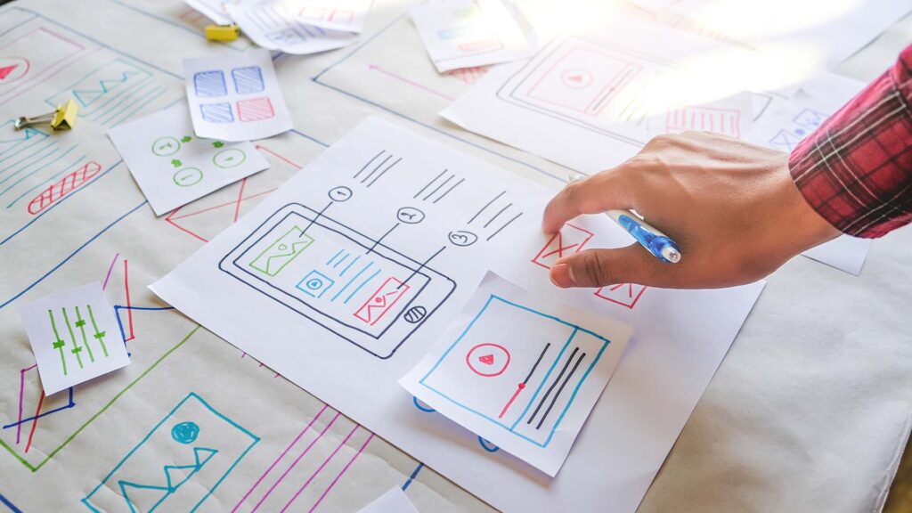 Close up ui/ux designer working and designing a user interface for website and application, researching, planning and brainstorming by sketching ideas and designs with paper, pen and pencil.