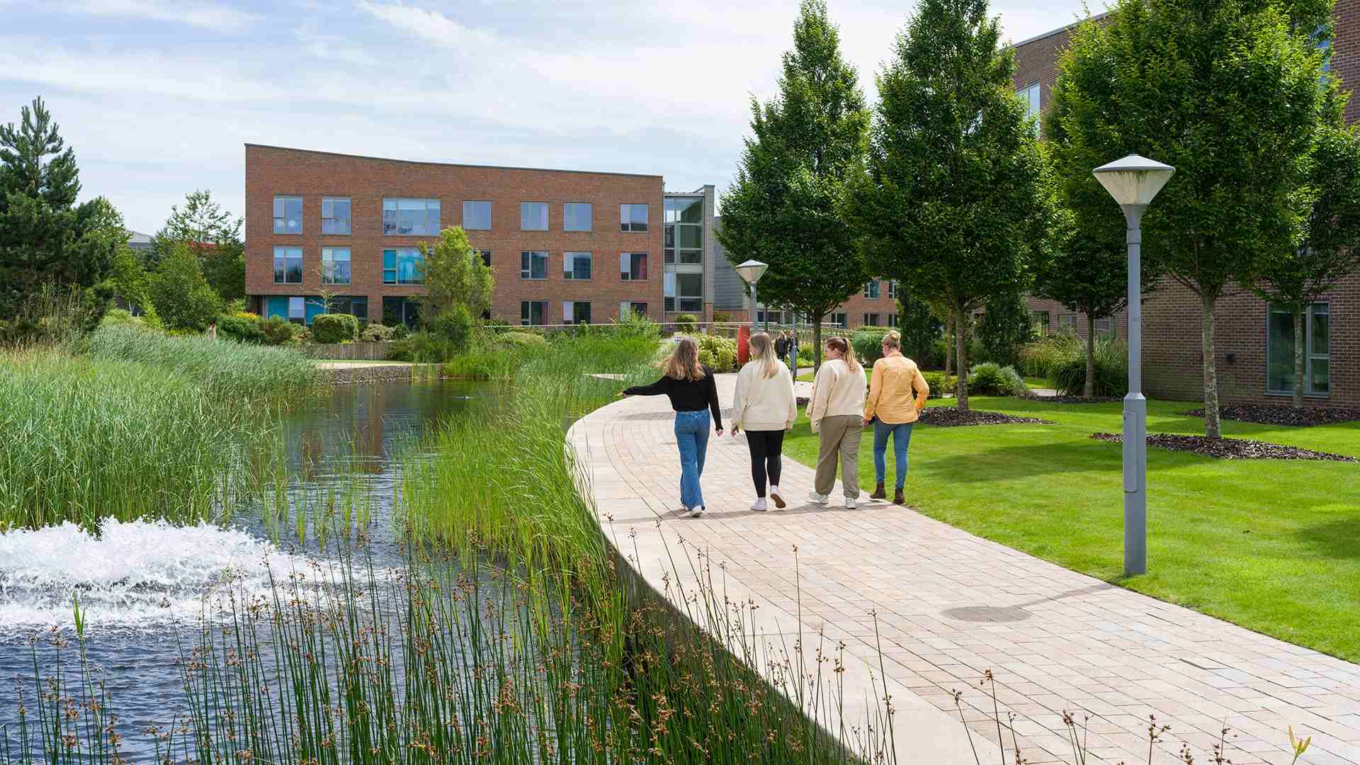 Students walk across campus beside the lake close to Chancellors Court accommodation and Creative Edge.