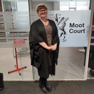 Photo of Bethan Ashton in wig and gown stood outside the Moot Court Room at Edge Hill