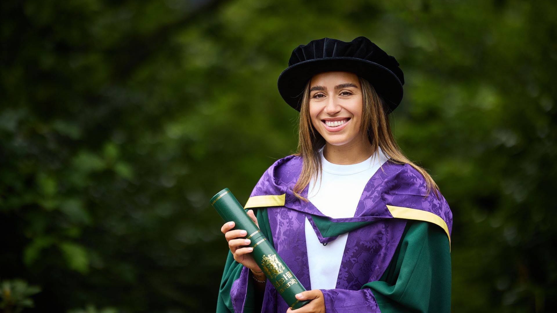 Chelcee Grimes wears her purple and green gown and holds a green scroll case.