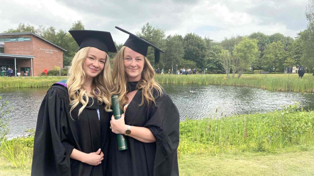photo of mum and daughter outside EHU lake with their graduation gowns smiling.