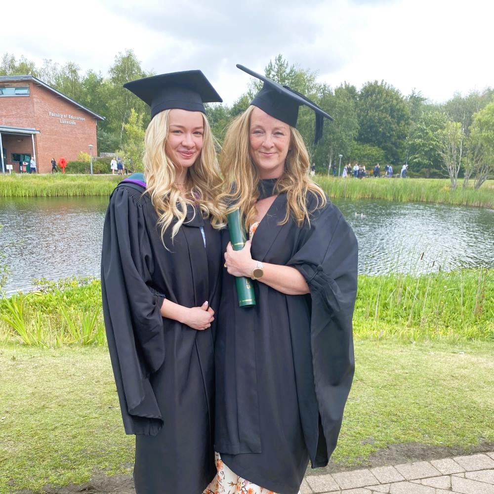 photo of mum and daughter outside EHU lake with their graduation gowns smiling.