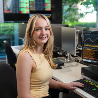 Isabelle Hudson sat at desk with computer screen showing Bloomberg software.