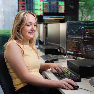Isabelle Hudson sat at desk with computer screen showing Bloomberg software.