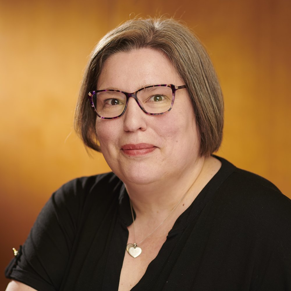 Portrait of Rebekah Pritchard wearing a black top with leopard print glasses smiling to the camera. 