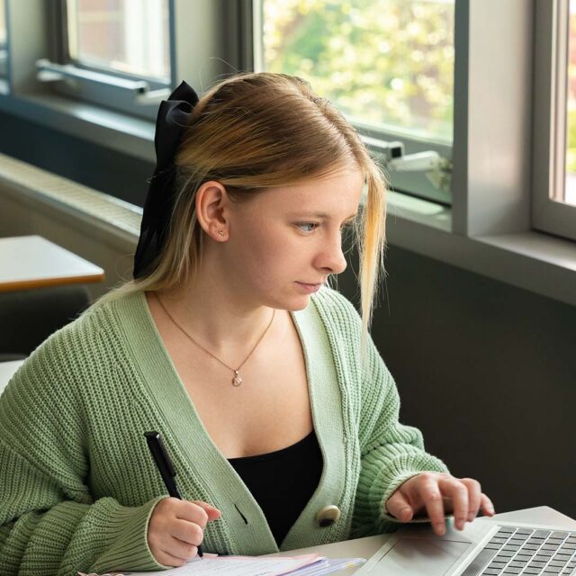 Student studying using a laptop and a notepad and pen