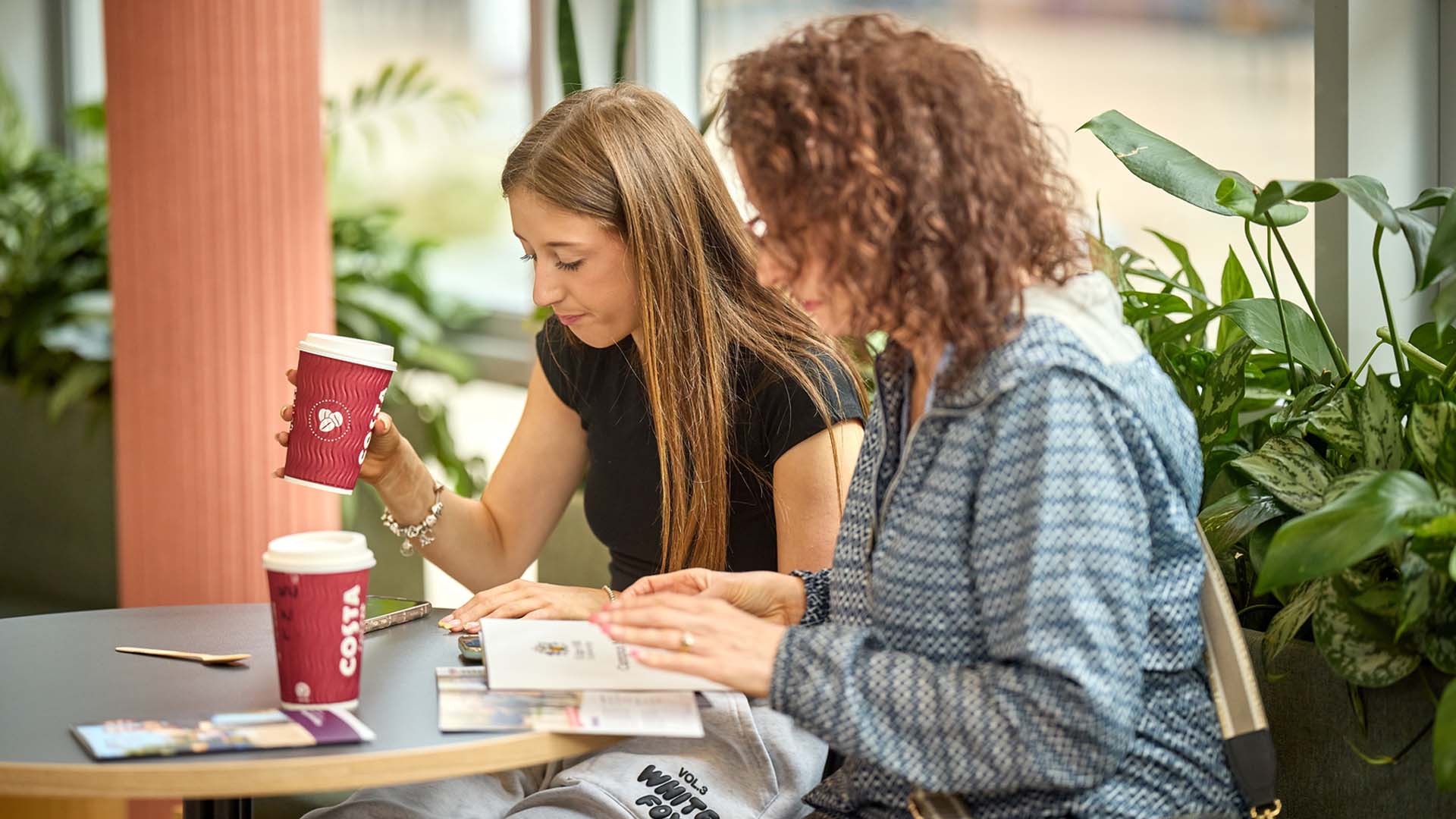 Image of visitor with their parent/supporter in the Hub reading materials at an open day