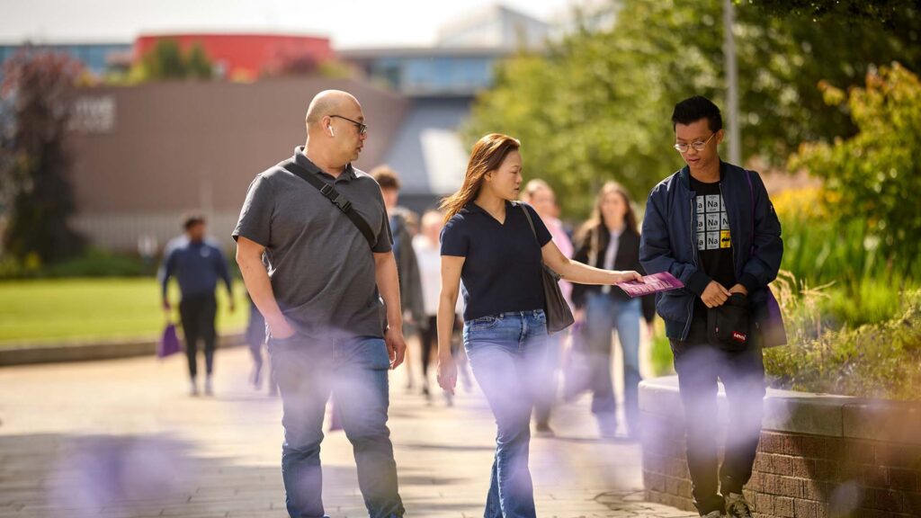 Image of an open day visitor with their parents/supporters. They are walking outside of the Hub with Creative Edge in the background behind them