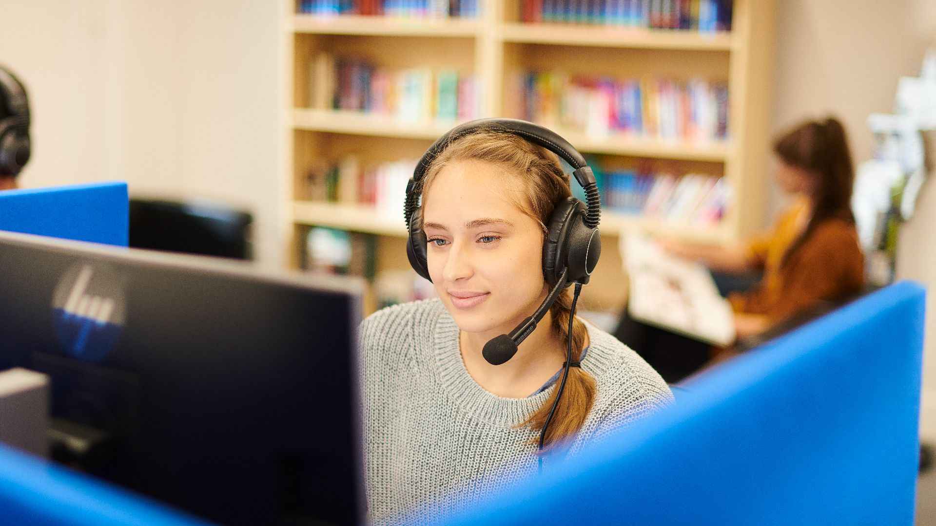 Student wearing headphones and a microphone while working on a computer.