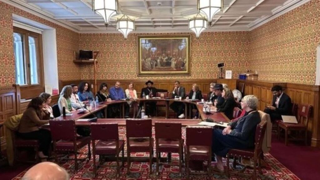 a room in the house of lords with 19 people sat around in a circle talking to each other. 