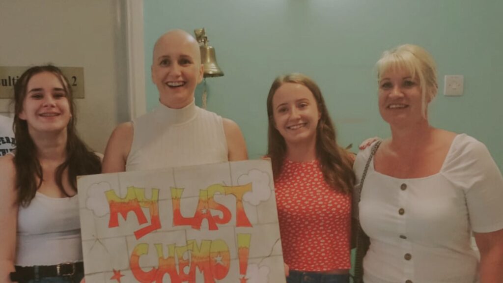 Carol with her two daughters and a friend, carol is holding up a sign that says my last chemo