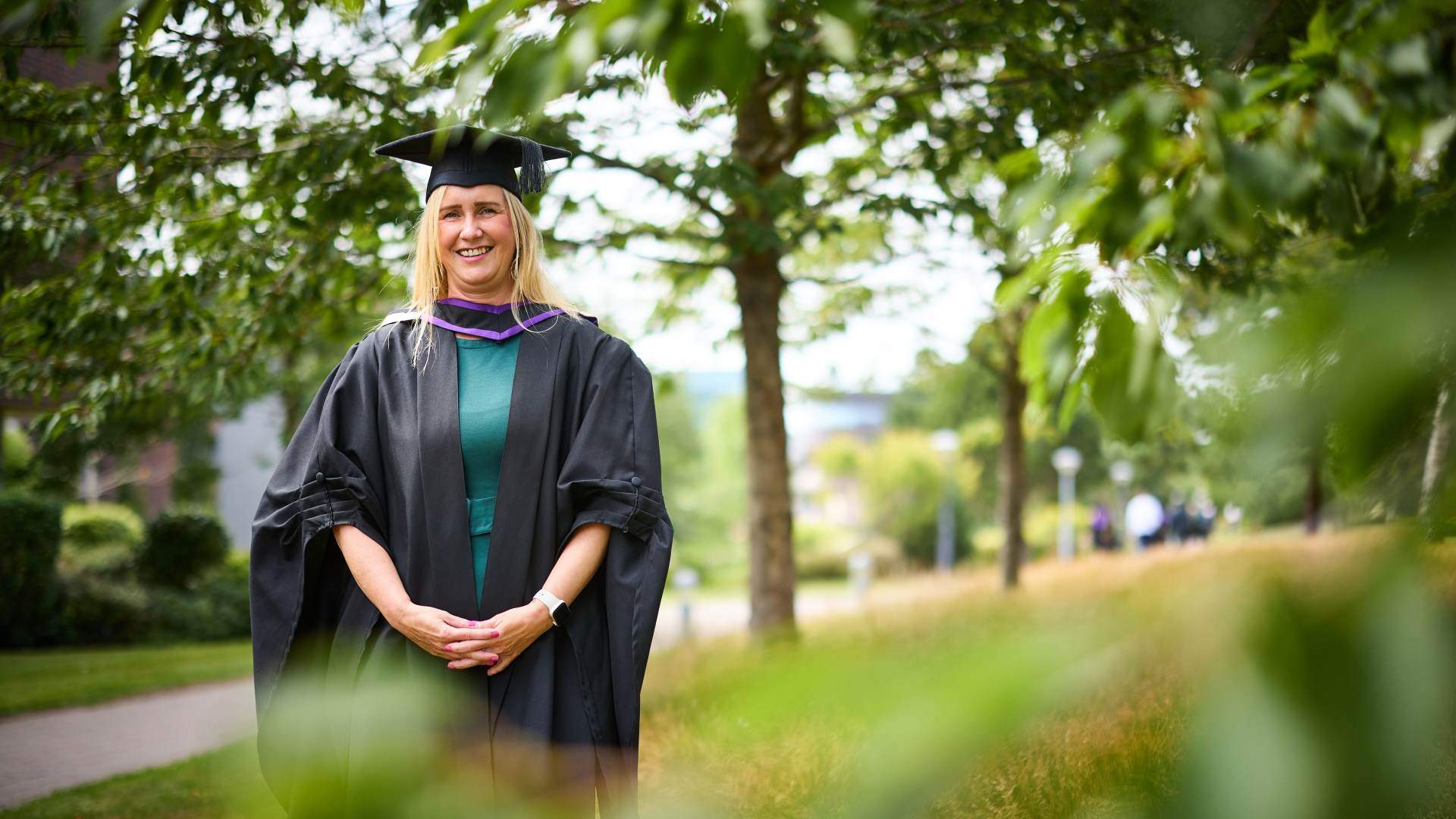 Graduate Carol Kenntete standing outside looking at the camera in her robe and cap.