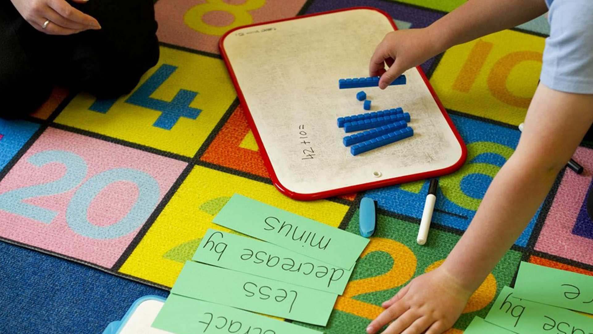 Close up photo of a teacher and student working on maths problem in a classroom environment.