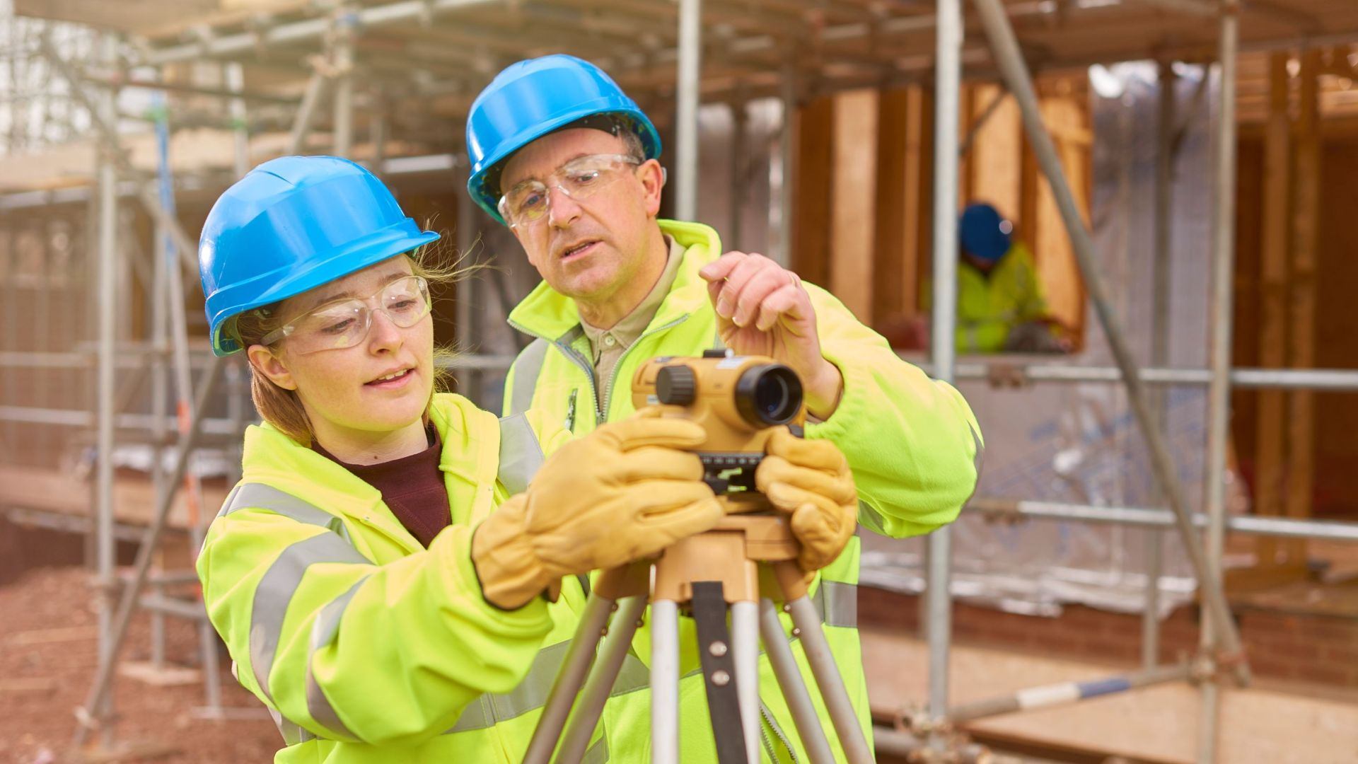 A student and a professional on a building site wearing high vis vests and helmets.