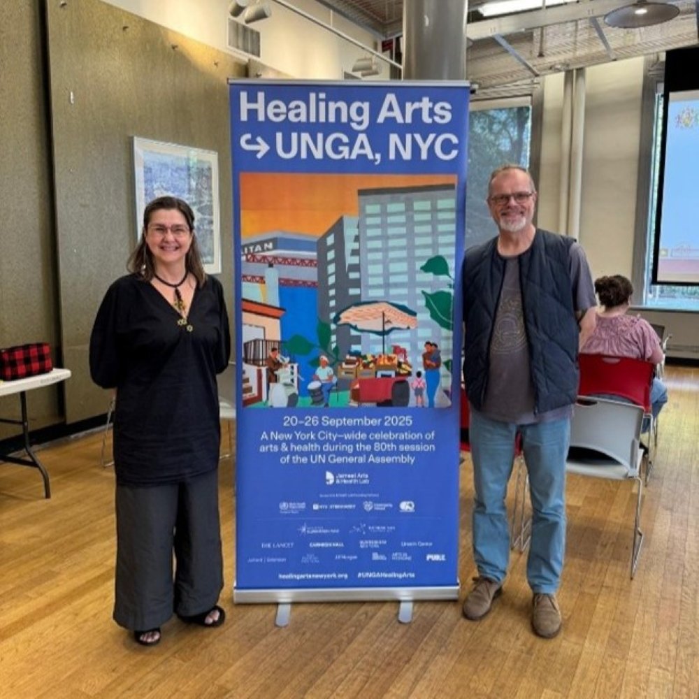 Professor Vicky Karkou standing in front of a blue banner that says healing arts UNGA, NYC with another attendee. 
