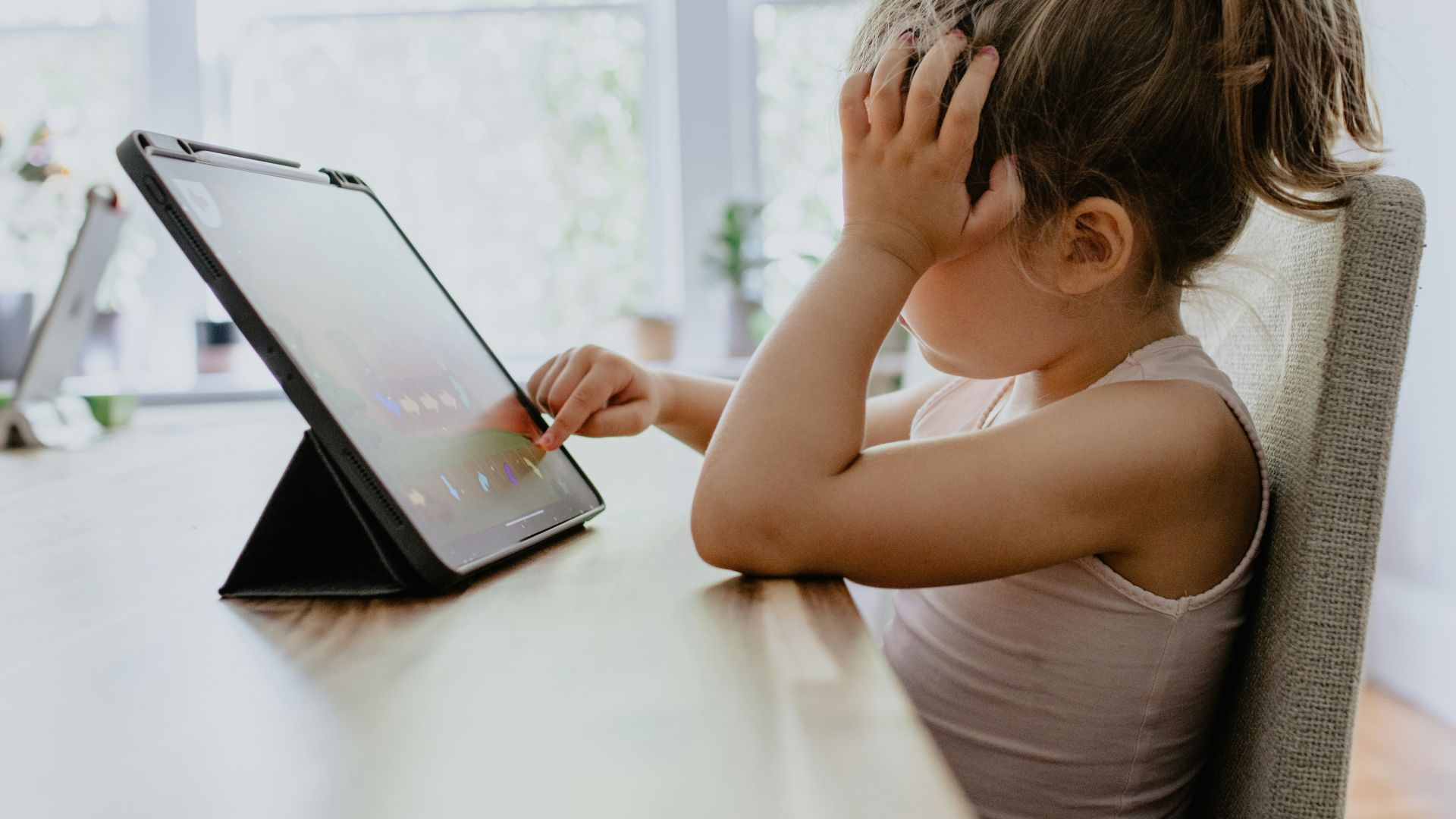 child playing game on ipad with hand on head.