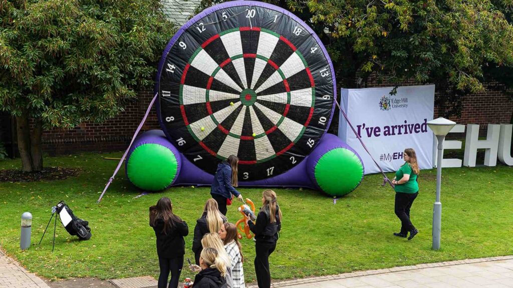 Very large inflatable dartboard on the grass in the background and students stood in the foreground 