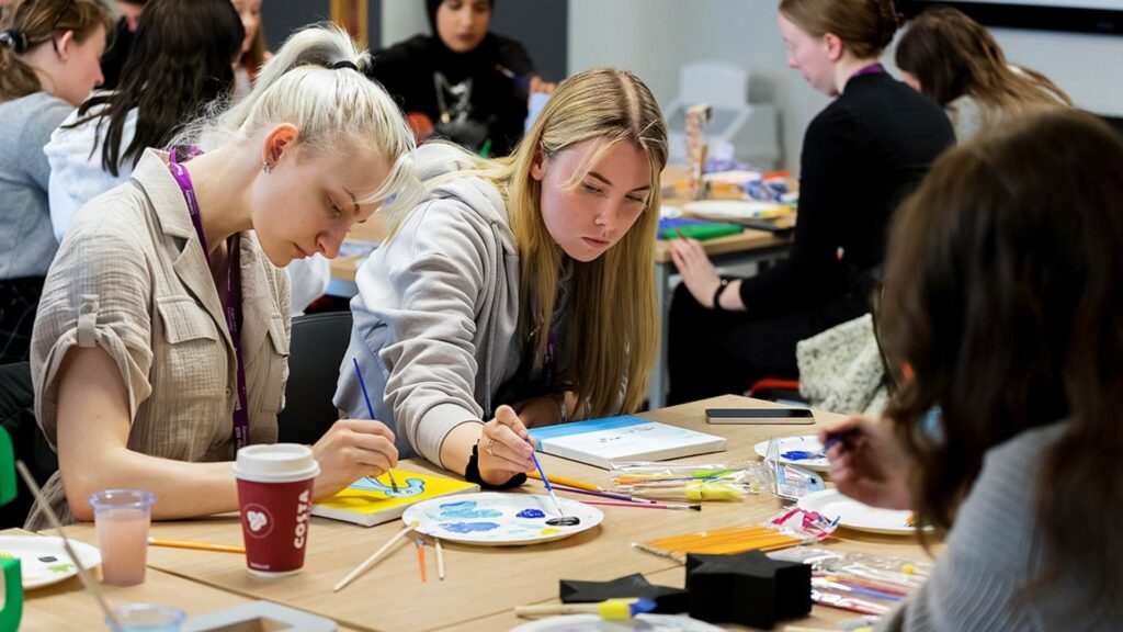 A group of students sat at a table painting on small canvases