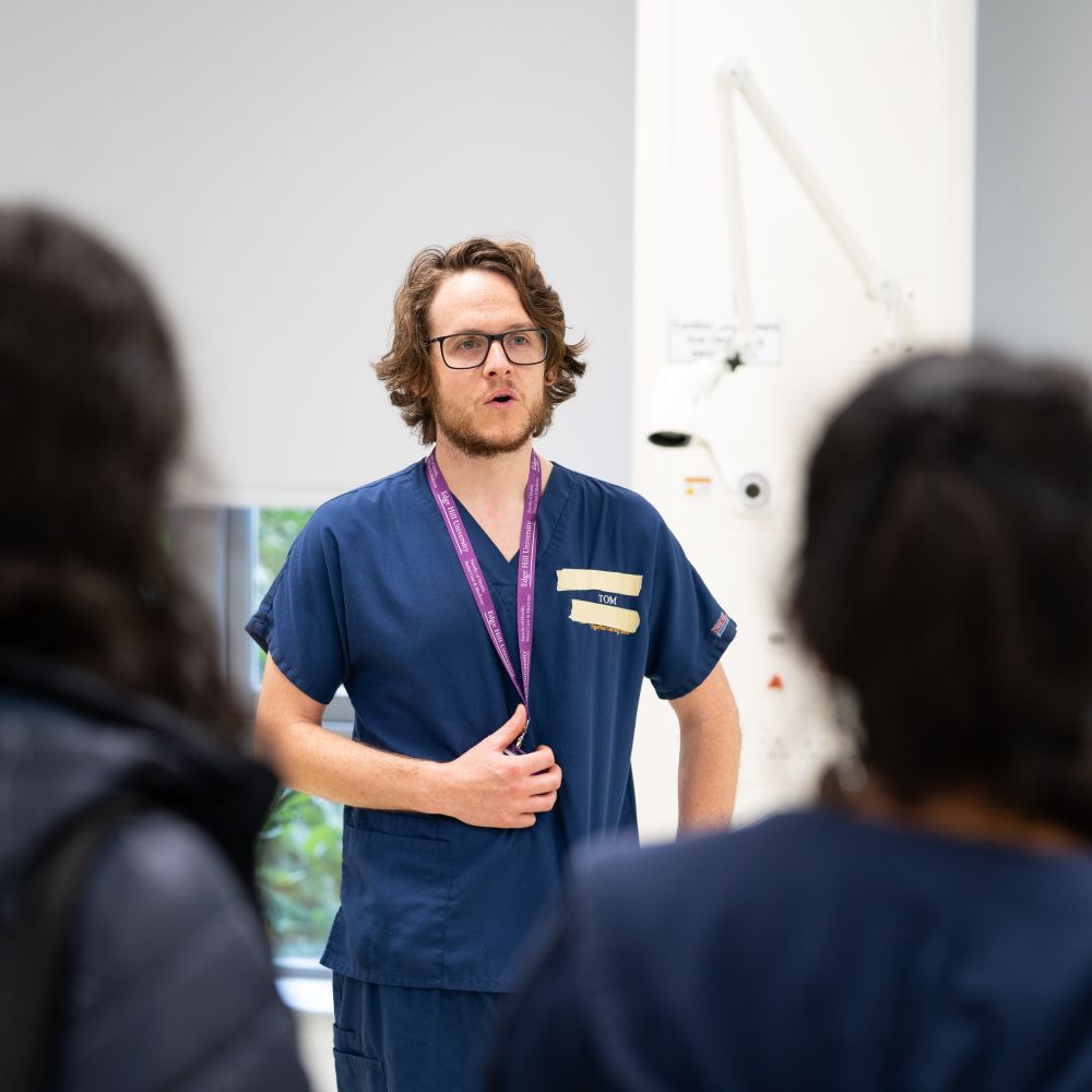 A doctor wearing scrubs and a lanyard presents to students
