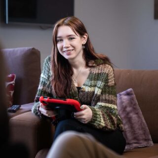 Student sat on a sofa holding an electronic device