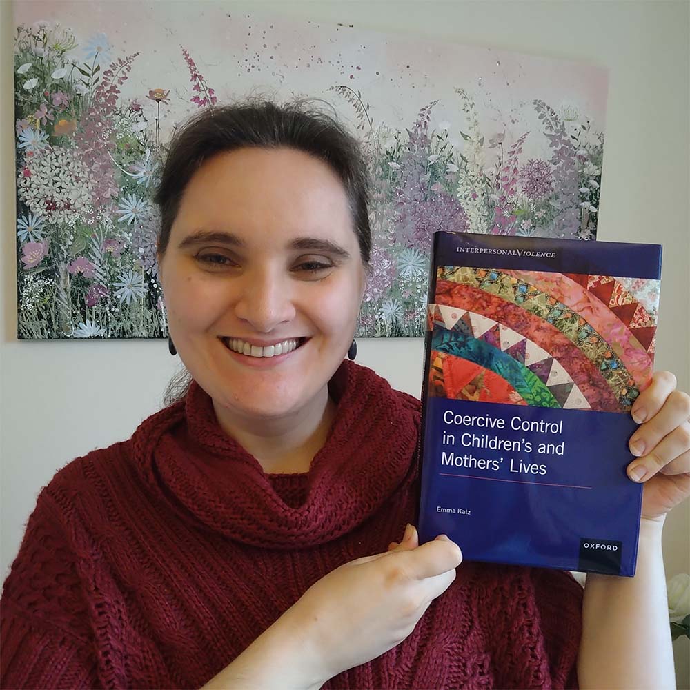 Profile photo of Dr Emma Katz holding a copy of her book 'Coercive Control in Children's and Mothers' Lives'.