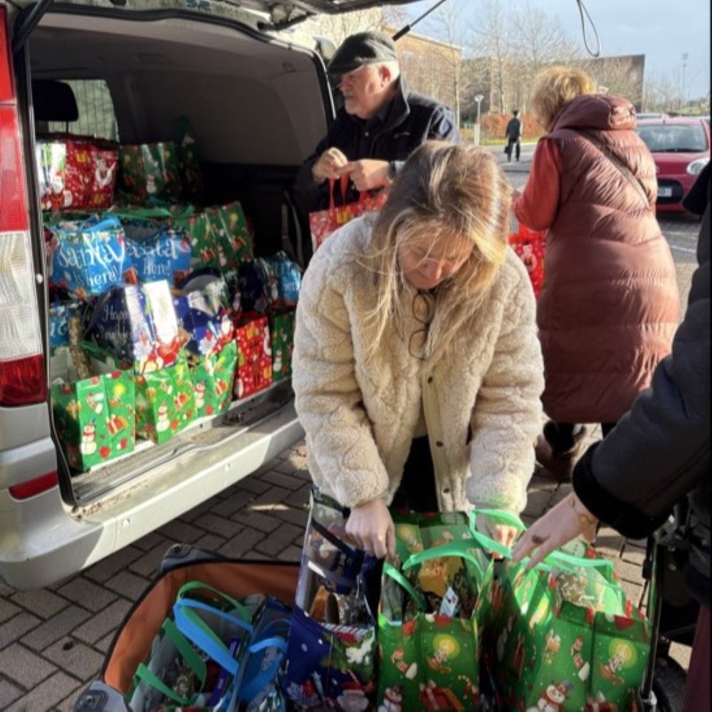 Woman taking hamper bags out of car and placing them on trolly. 