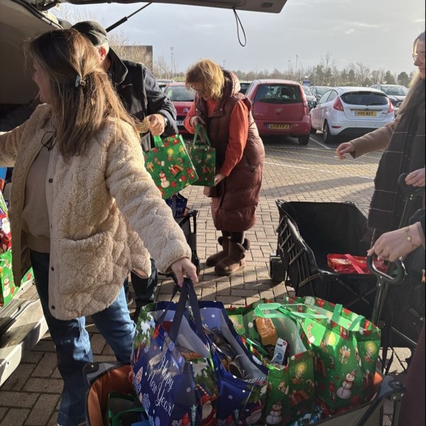 Woman taking hamper bags out of car and placing them on trolly.
