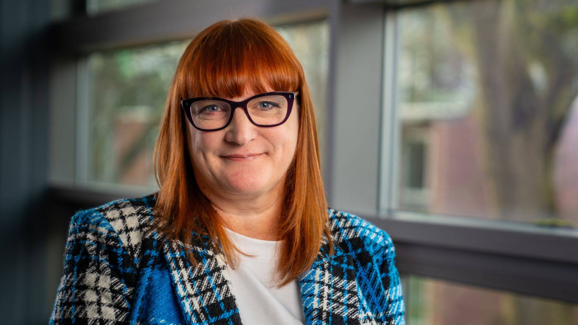 Dr Jo Wright stands in front of windows and smiles at the camera