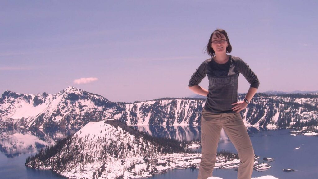 A person stood at the top of a high edge, with a scenic mountain scape behind them.
