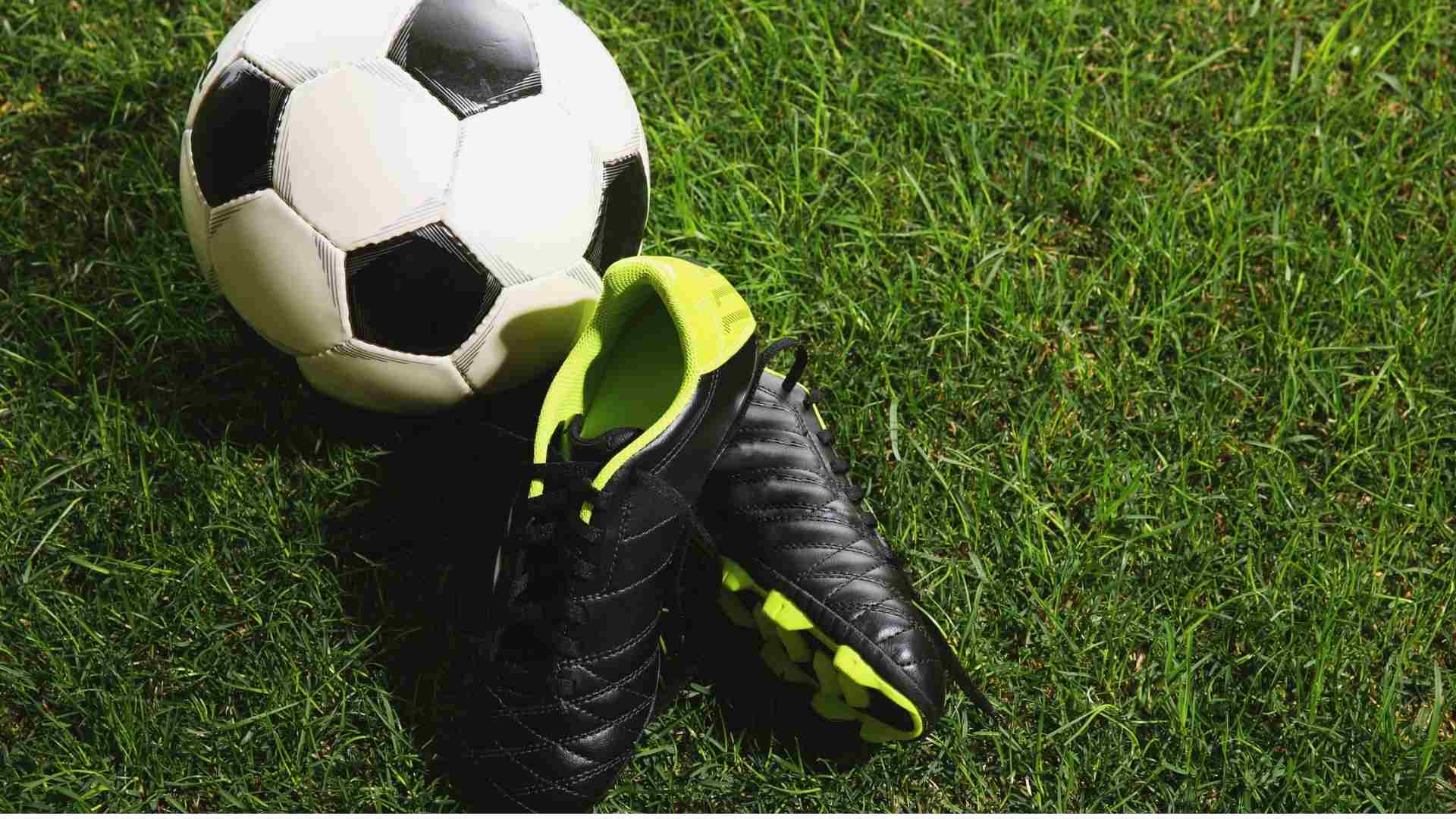 Football boots and a football on a grass pitch