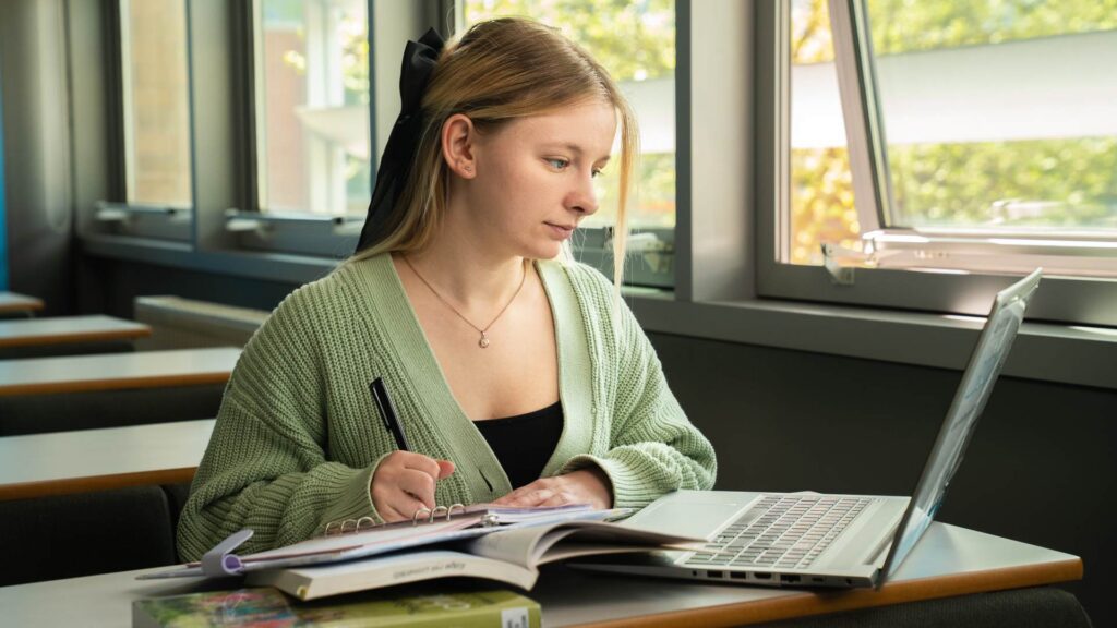 A student works at a laptop surrounded by books and a notepad