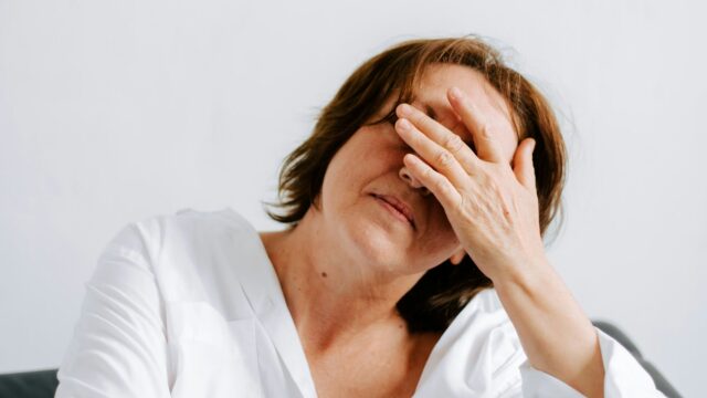Woman wearing white shirt with hands on face looking down