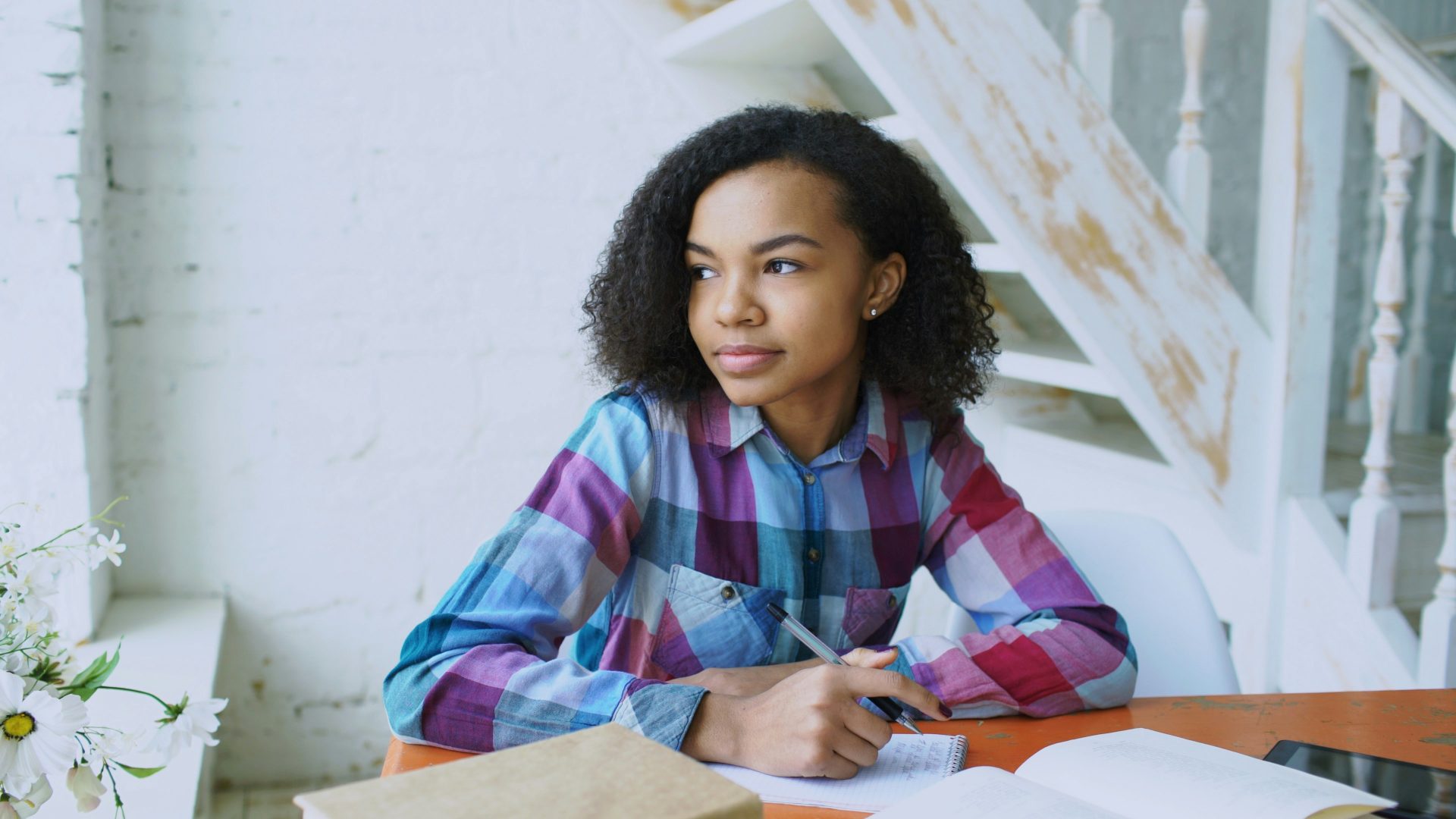 young woman wearing colourful checked shirt looking outside the window.