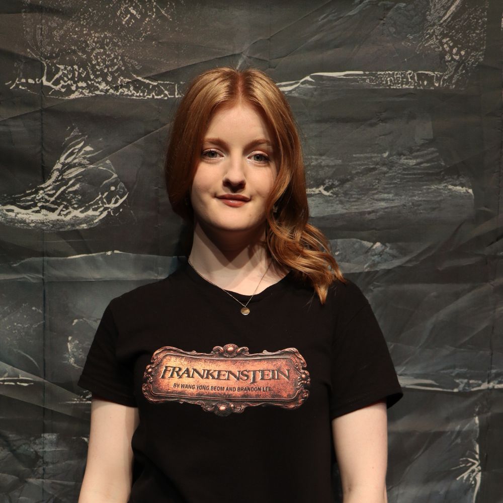 photo of student Alice standing behind black wall with Frankenstein Tshirt on