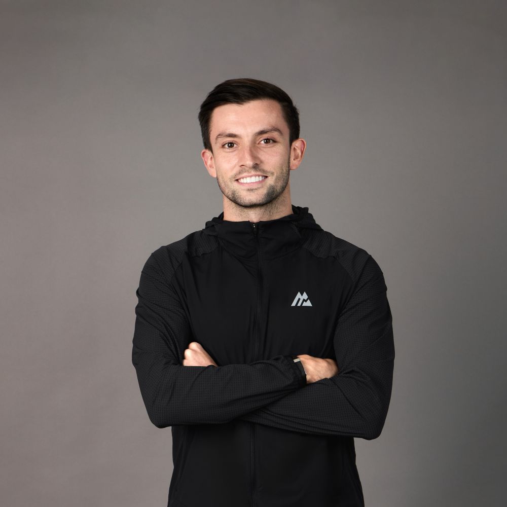 A man wearing black sportswear smiles with his arms crossed.