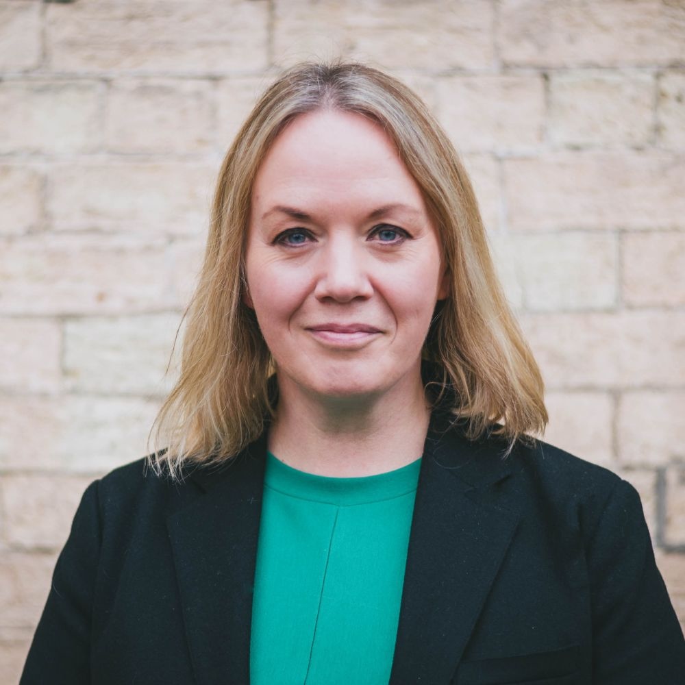 Hannah wearing blue top, black blazer behind a brick wall