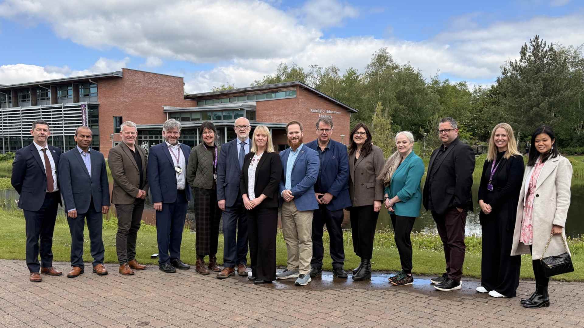 A mix of edge Hill staff and Northern Health Alliance standing outside lake at Edge Hill campus