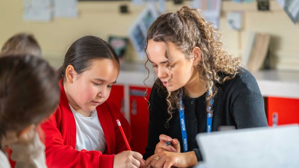 Teacher and primary aged pupil sat at table in classroom setting 