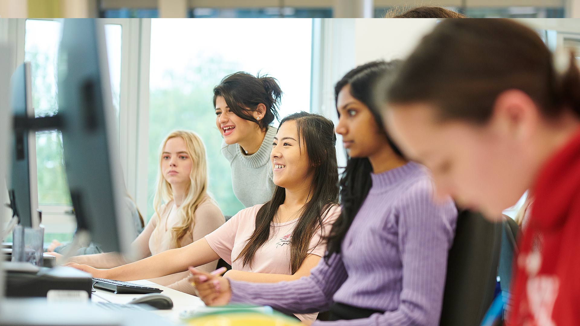 Female Computer Science students enjoying being taught by their tutor in the computer suite
