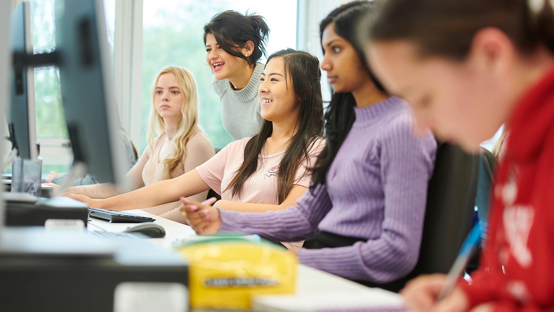 Female Computer Science students enjoying being taught by their tutor in the computer suite