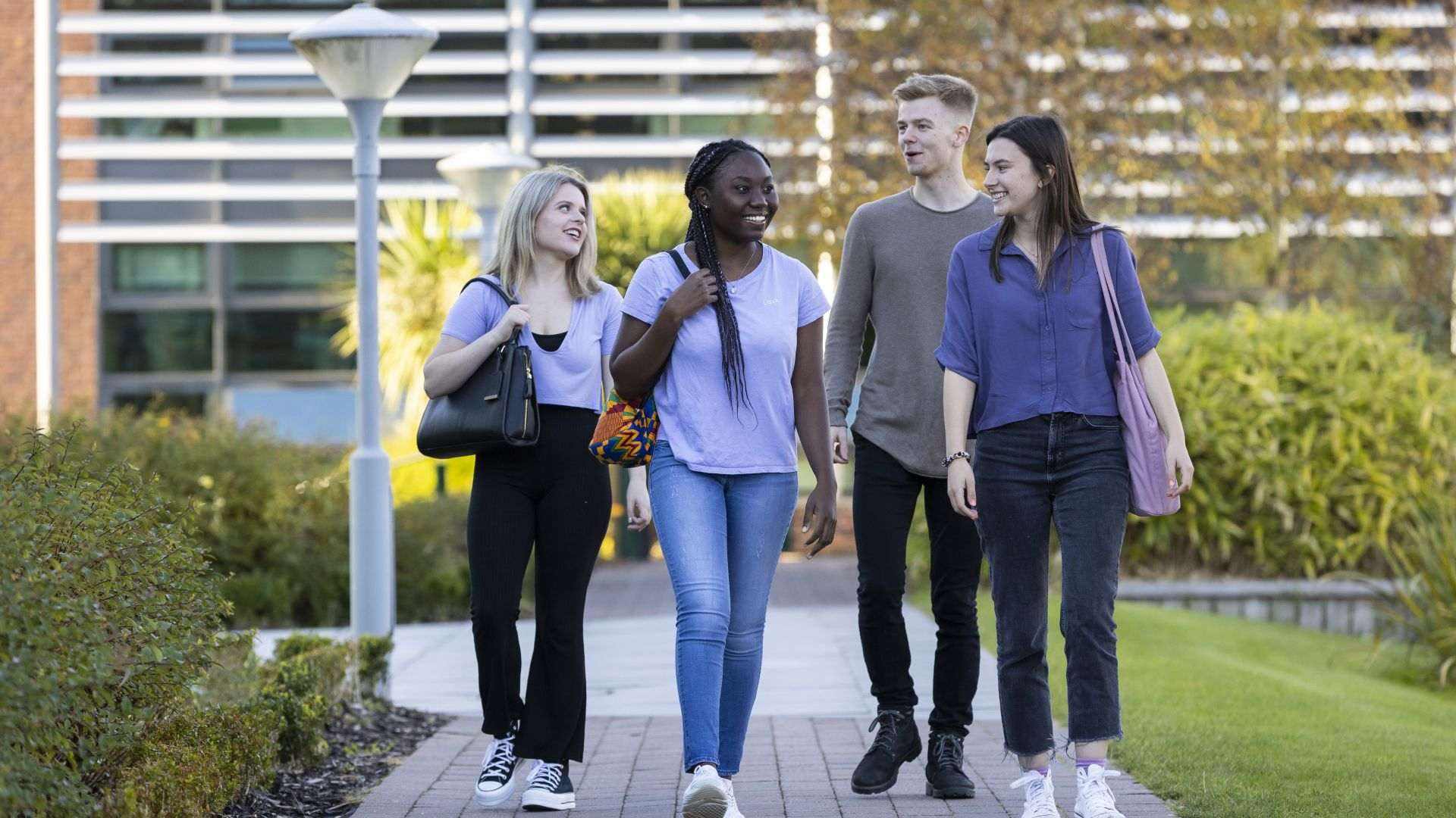 Four students walk along a path talking and smiling at each other.
