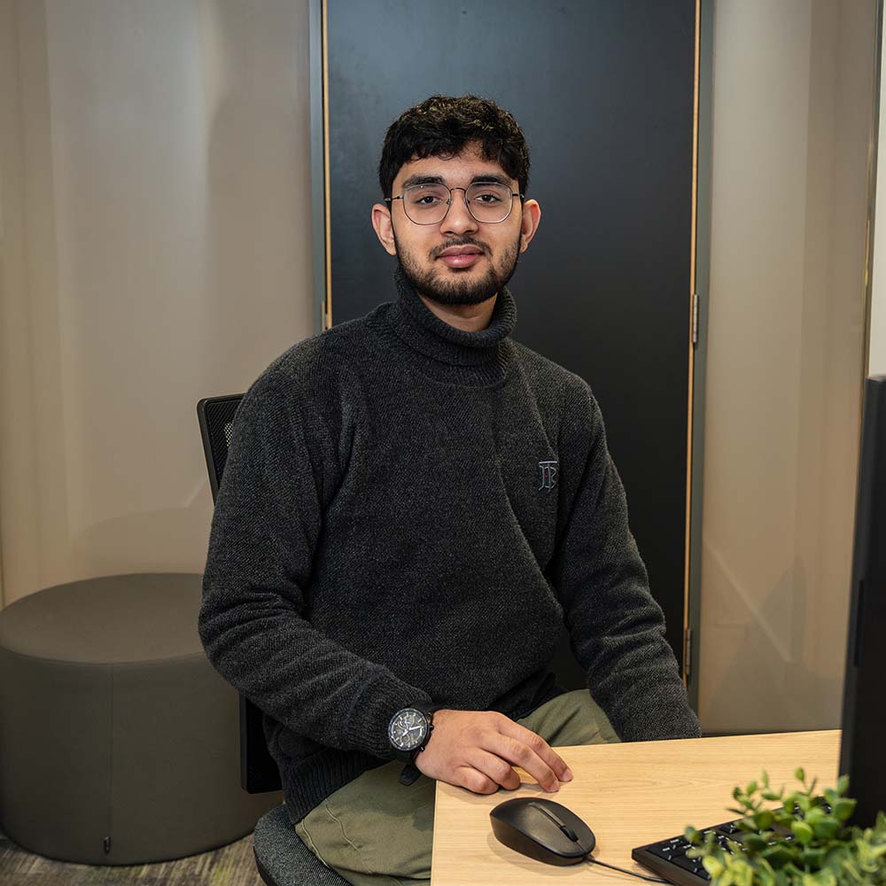 Student Taha sits at a desk in a study space, using a computer with a mouse and keyboard.