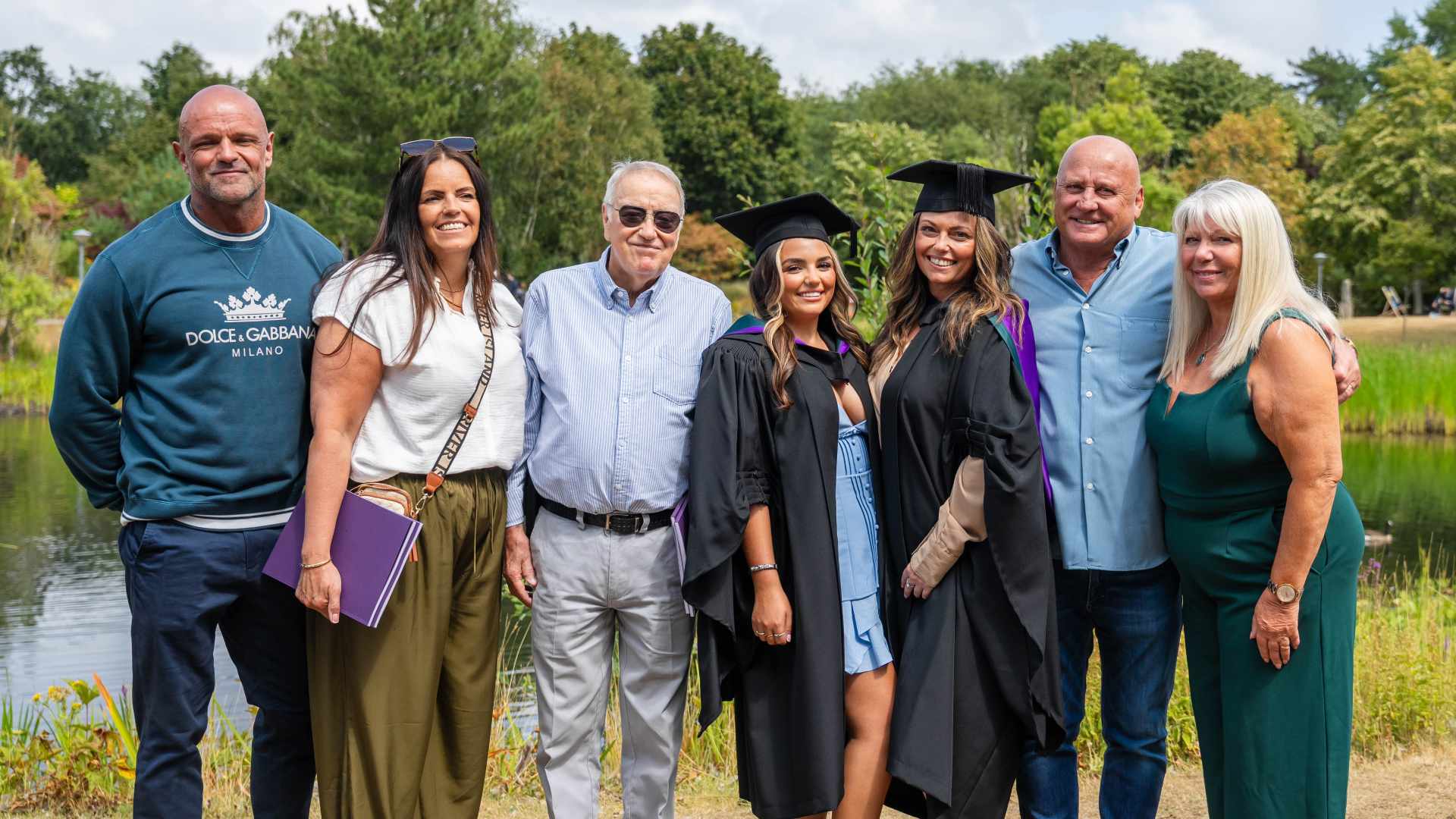 A group of people gather together in front of a lake and smile at the camera.