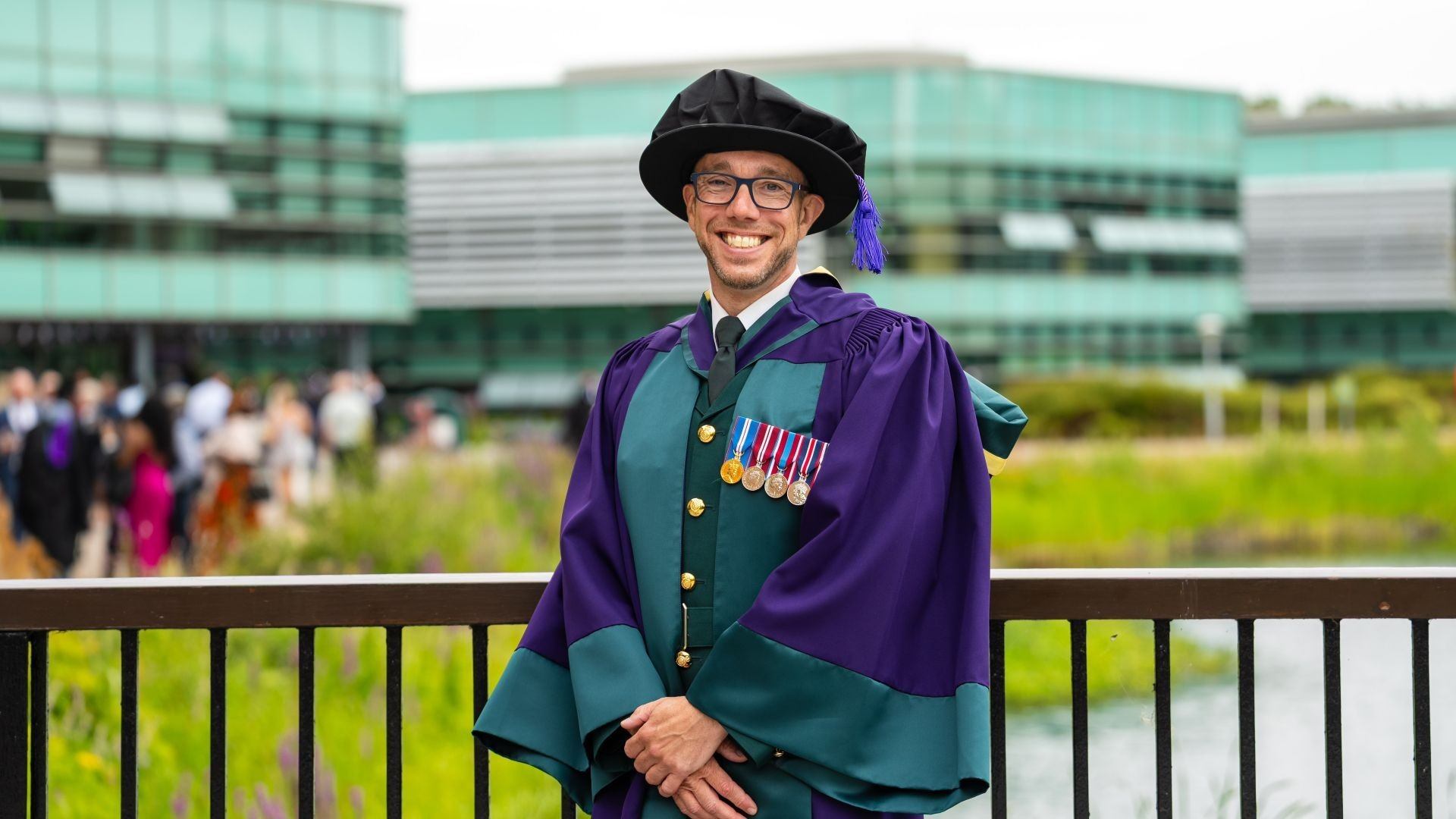 Dr Robert Till wears a green and purple gown with a black cap and tassle.